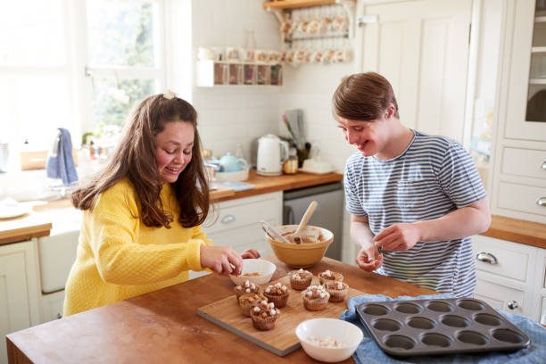 Young Downs Syndrome Couple Decorating Homemade Cupcakes With Marshmallows In Kitchen At Home